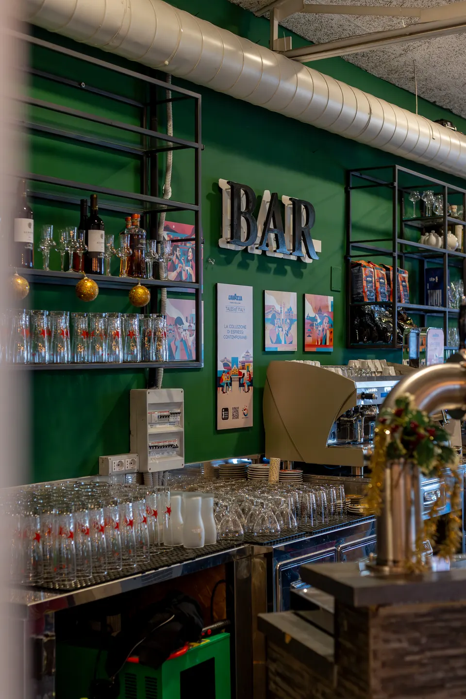 Il bancone del bar con la parete verde, l’insegna BAR e la spina della birra