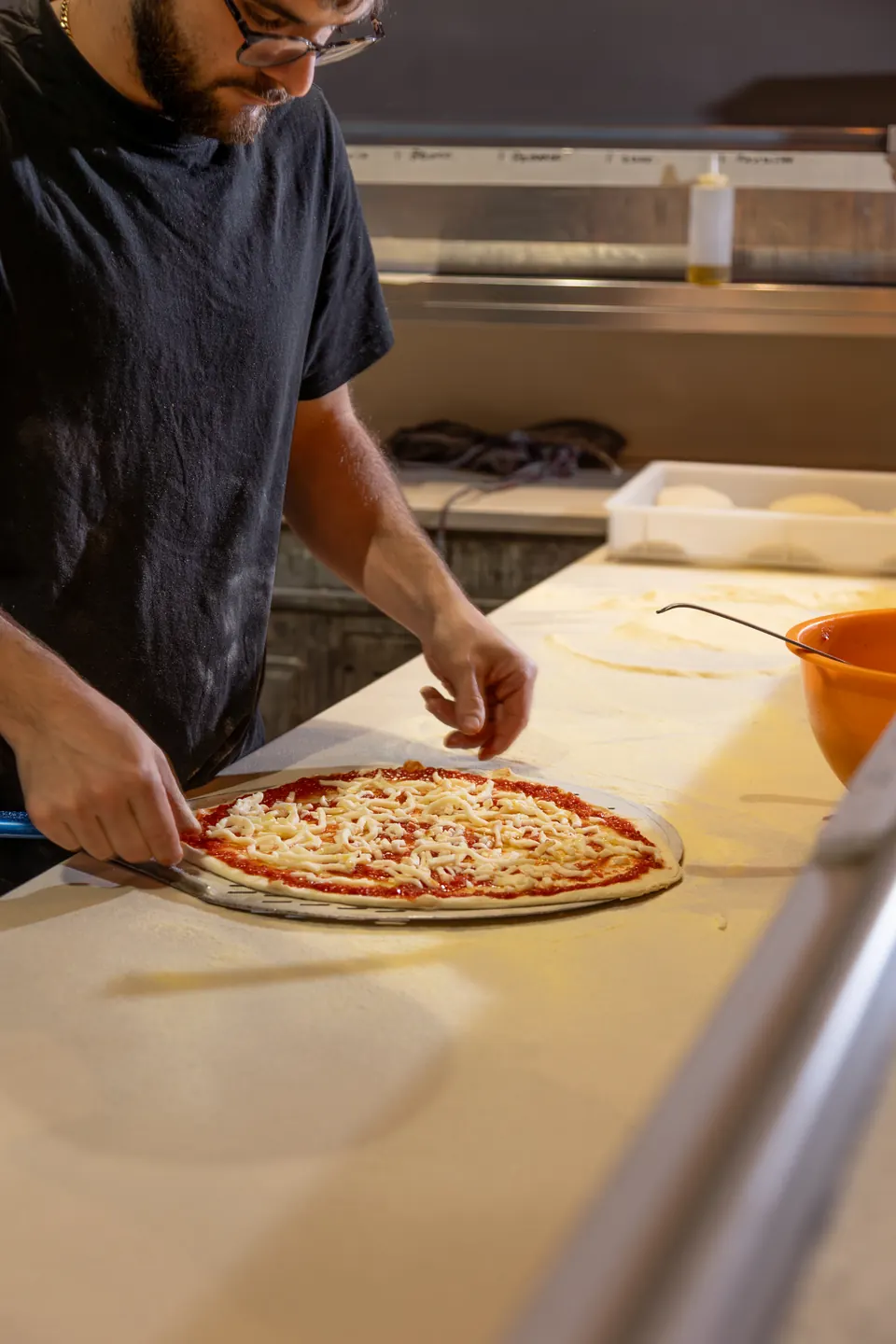Il pizzaiolo stende una pizza sul bancone