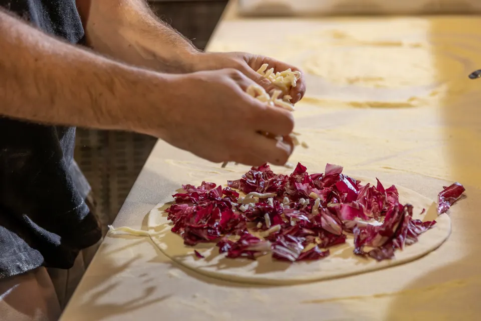 Mani che condiscono con il formaggio una pizza con radicchio