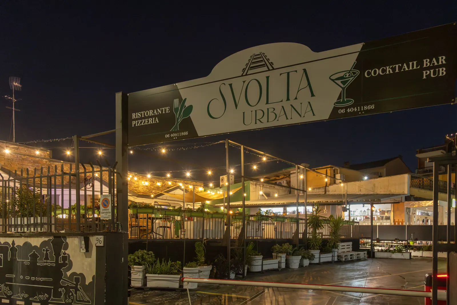 L’insegna di Svolta Urbana di notte, con le luci a festone della pedana sullo sfondo