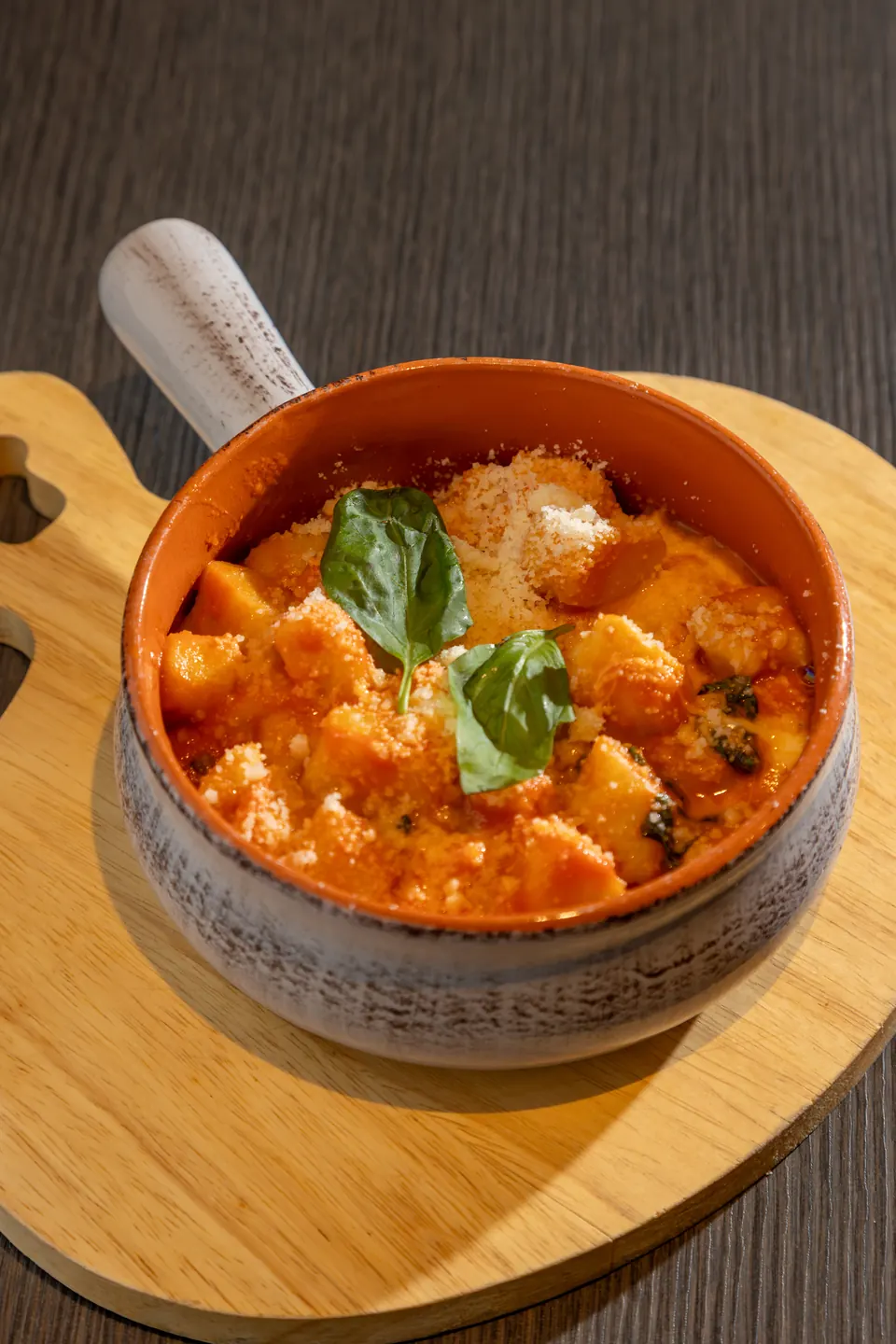Un piatto al sugo di pomodoro con basilico, servito in una ciotola su un tagliere di legno