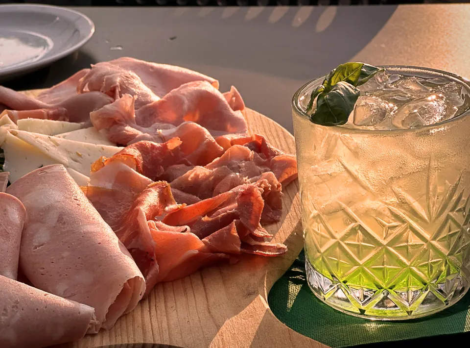 Un tagliere di salumi e, accanto, un bicchiere con ghiaccio e una foglia verde